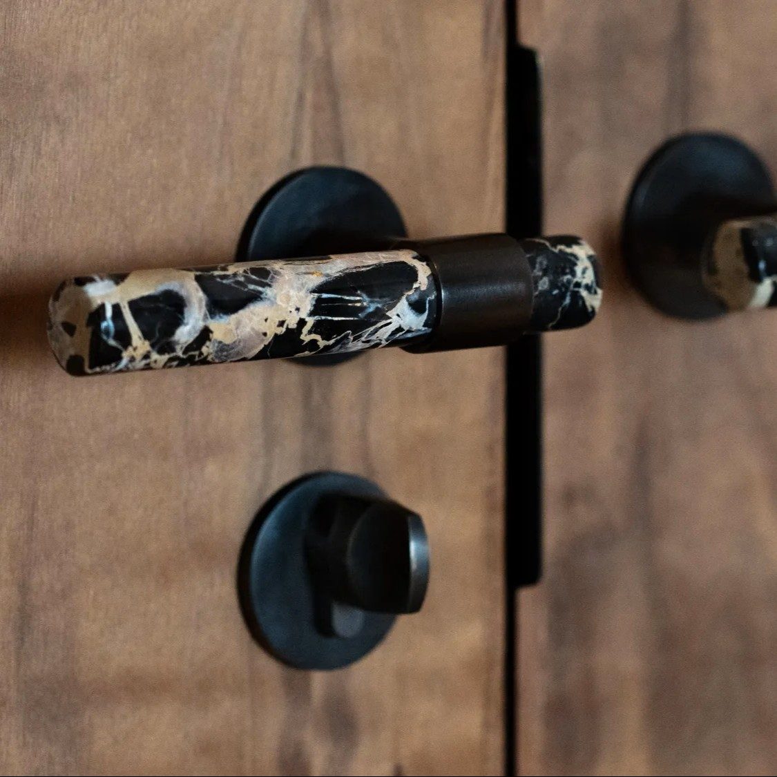 A black lever and thumb-turn mounted on a walnut door, photographed close.
