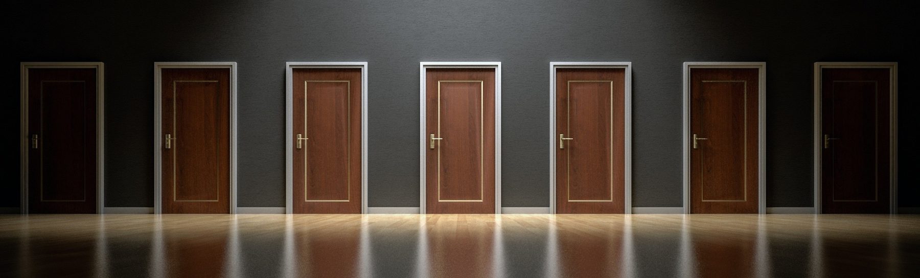 A row of six timber doors lit in a dark room, each one closed.