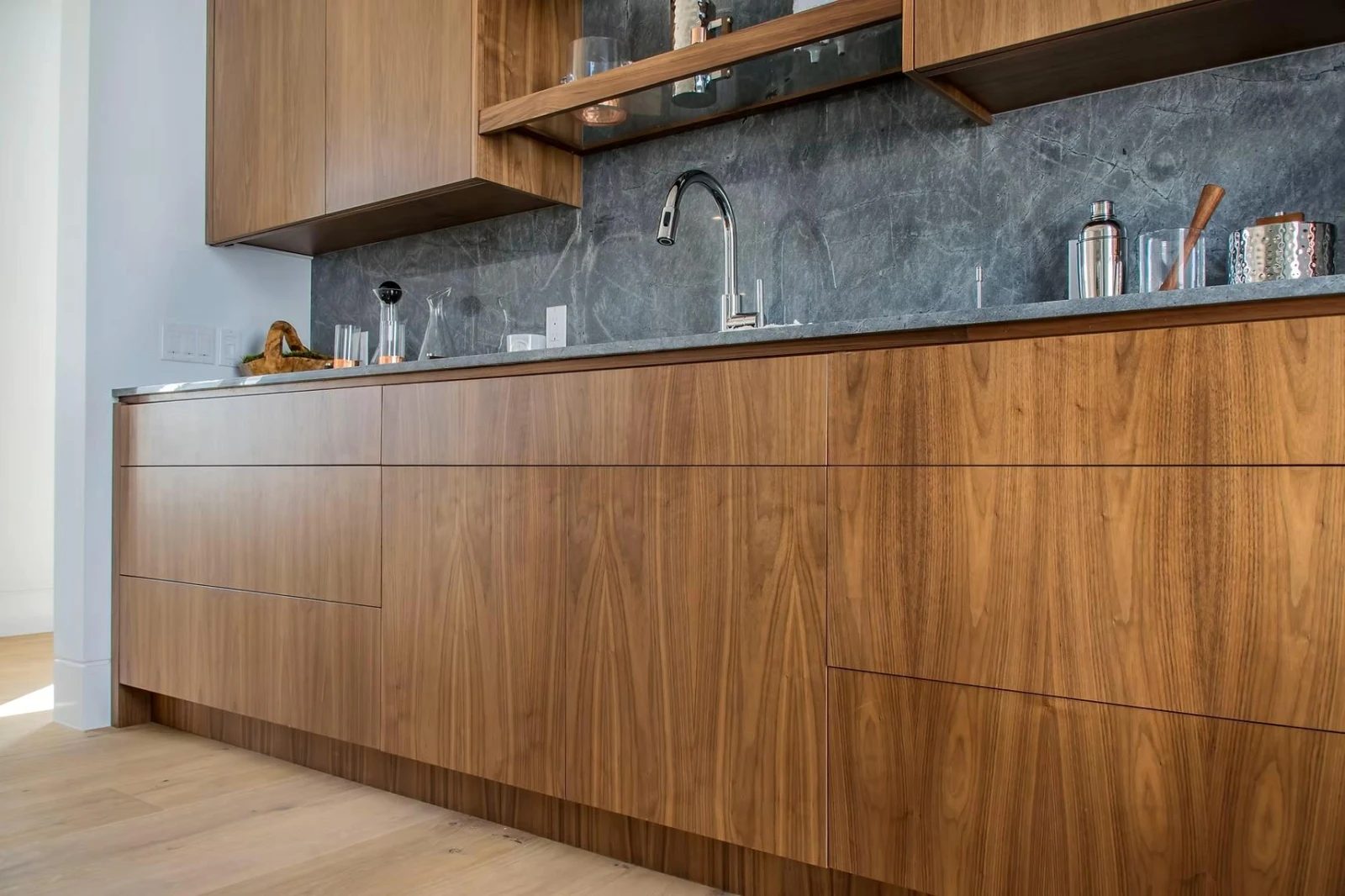 A walnut kitchen run with a stone splashback and open shelving, built by Fine Line.